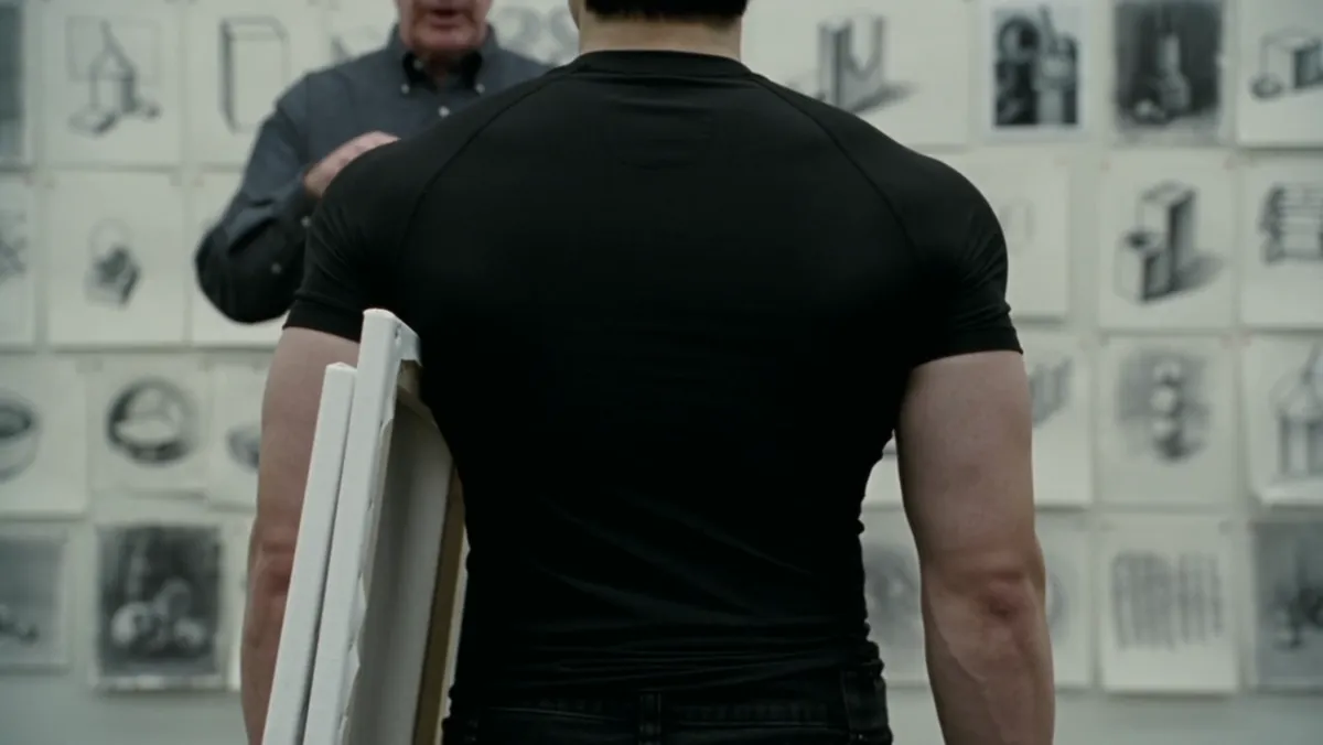 Seen from behind at a critique wall, boards held under one arm