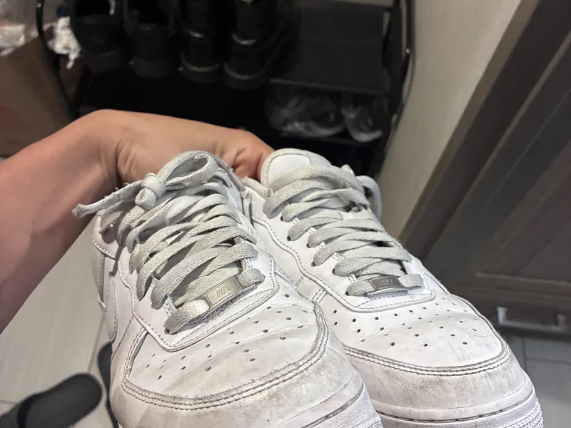 A hand holding a pair of white sneakers
